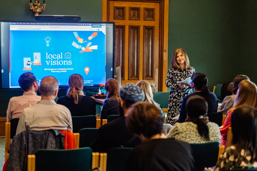 Claire Hardwick introducing Local Visions on a projector screen, in front on an audience