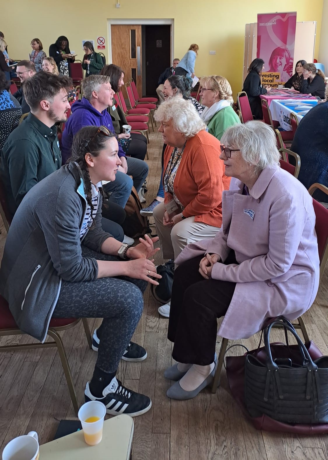 Northfield NNS Community Lunch in April 2023: a big room of people of all ages, facing each other on chairs and talking