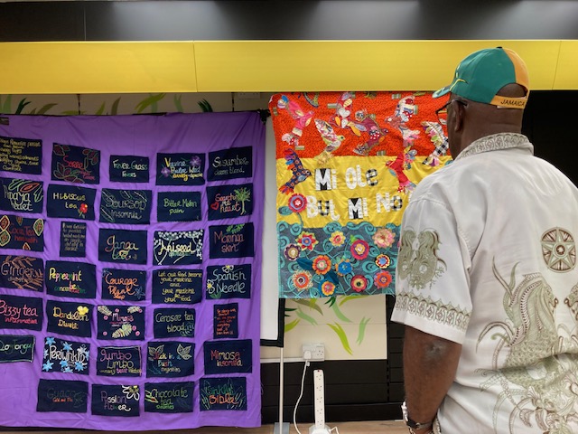 A man looking at colourful Windrush-inspired wall hangings, made by AAOTP members