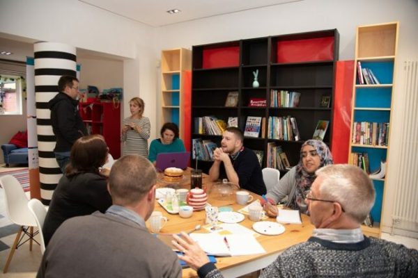 Eight people around a table with tea and cake, in a light and airy bookshop